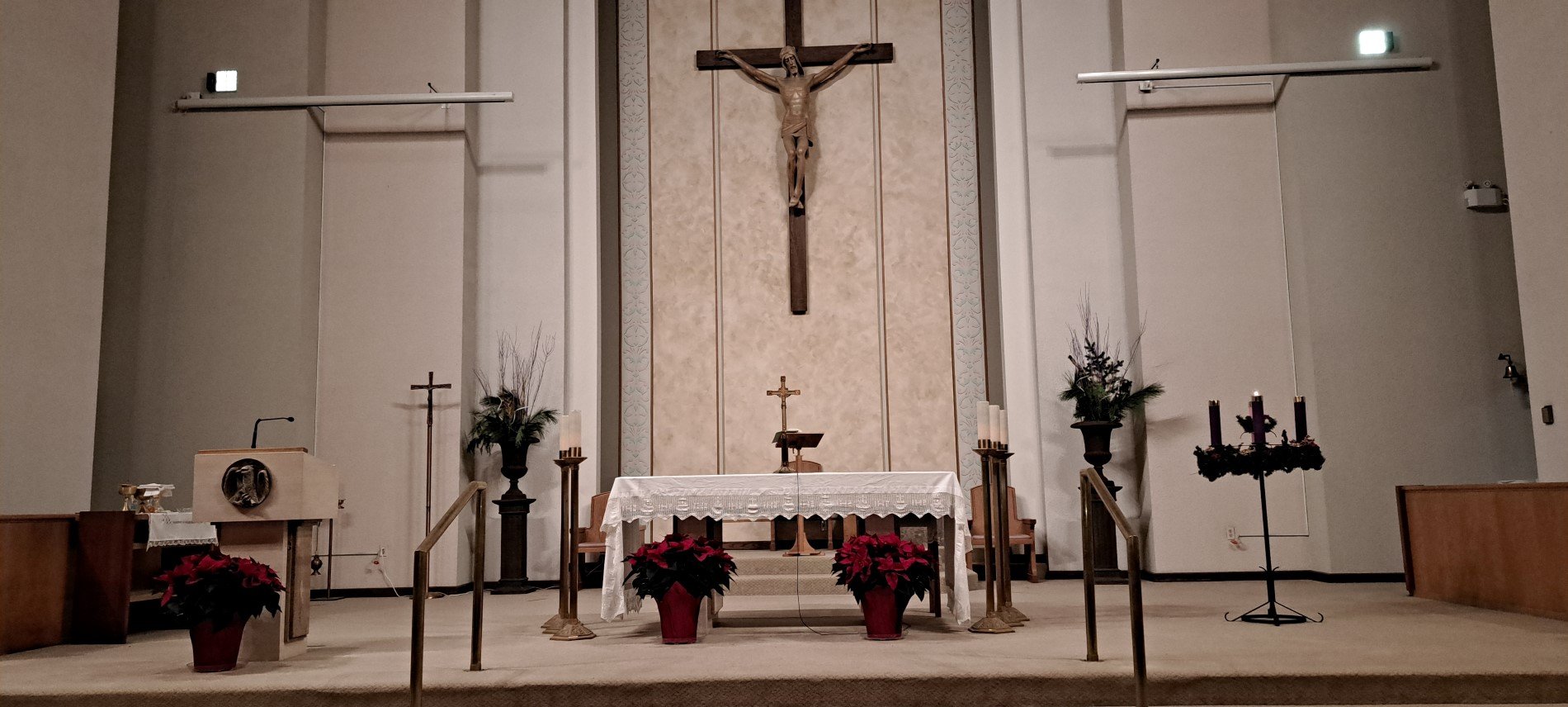 Picture of altar with poinsettia plants at base on altar and advent wreath to the right side