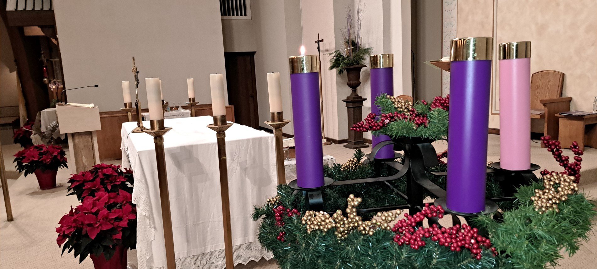 Picture of altar with advent candle wreath in foreground and poinsettia plants at base of altar