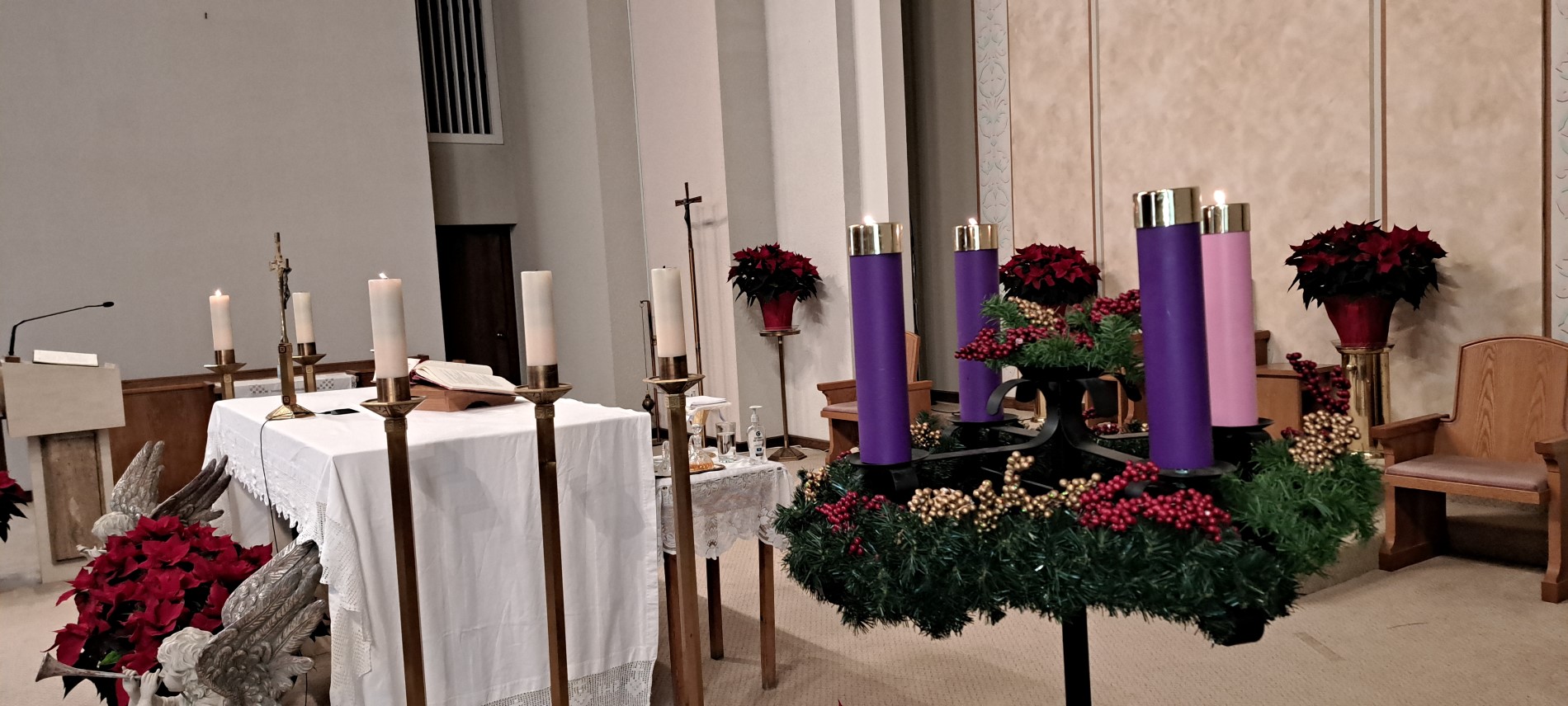 Picture of the altar with poinsettias and  3 candles lit on advent candle wreath