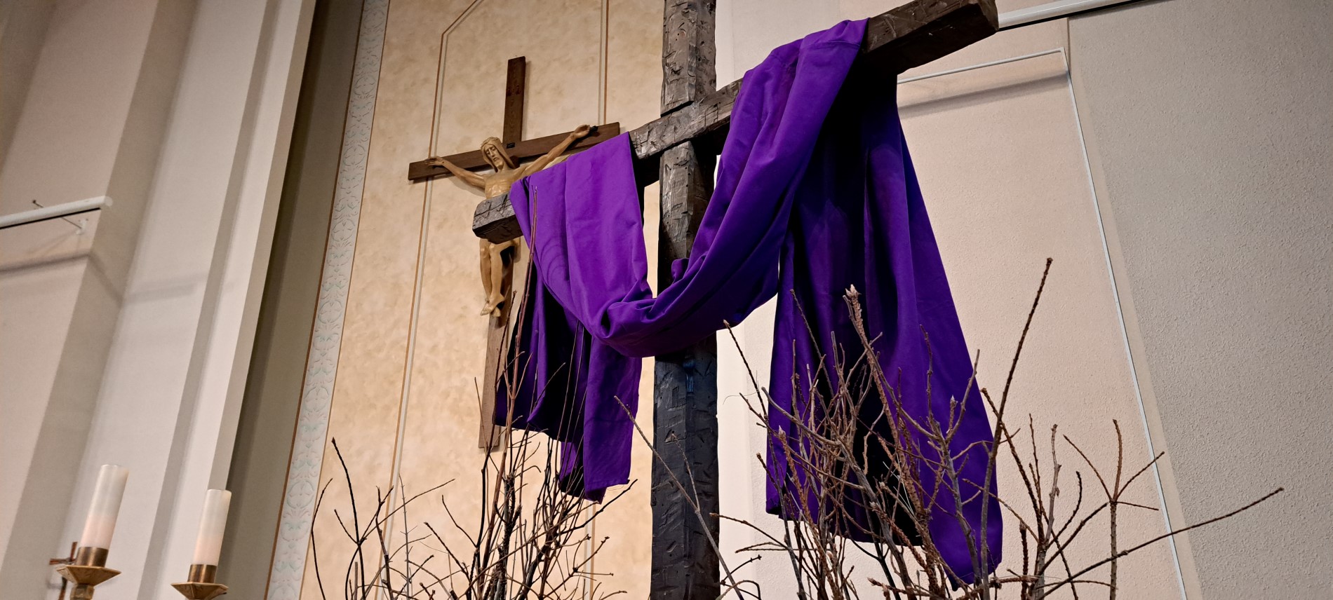 Picture of brown cross with purple cloth draped over and big crucifix in background