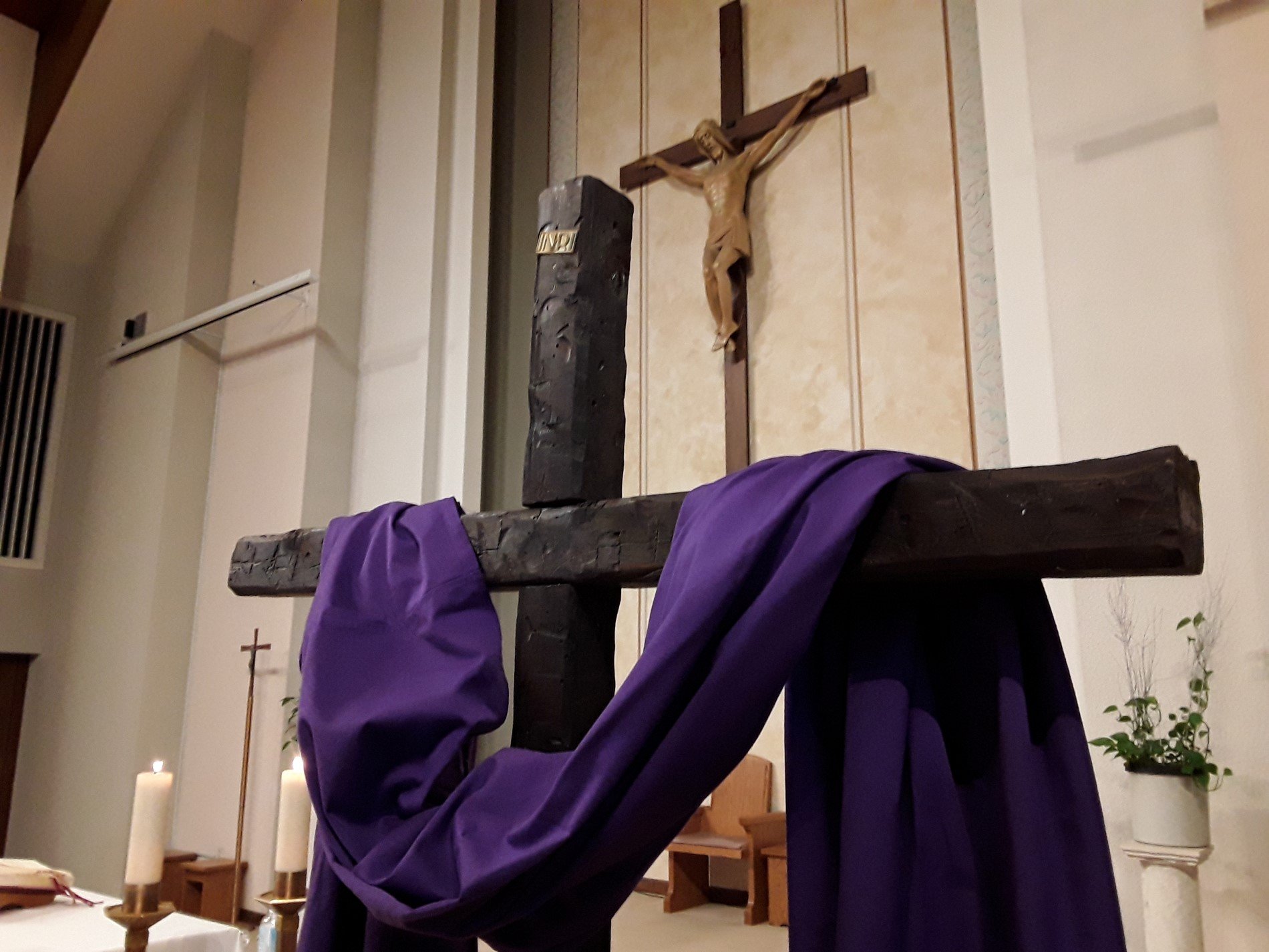 Picture of brown cross with purple cloth draped over and big crucifix in backgound